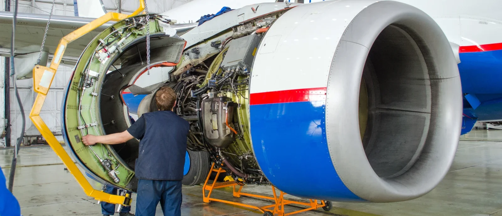 Aviation mechanic opening a jet engine cowling during maintenance in a hangar