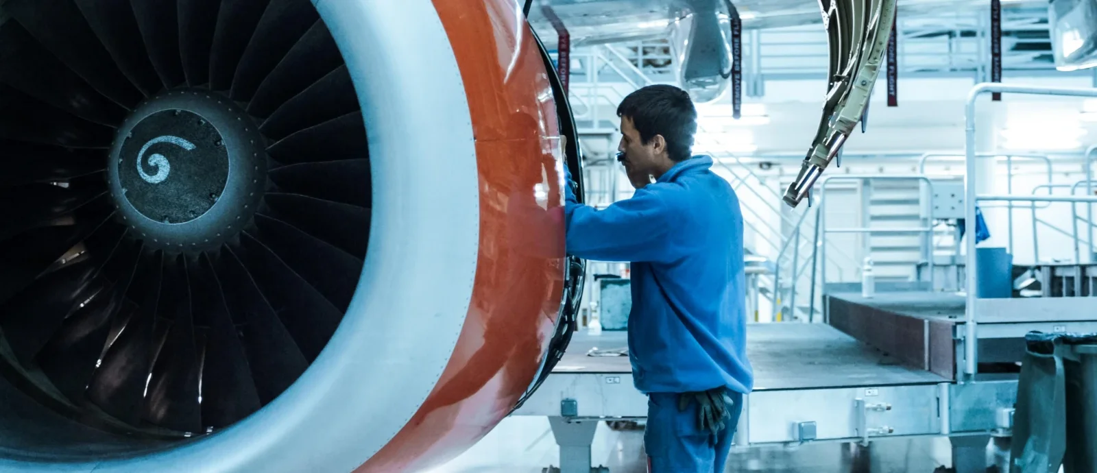 Aviation mechanic working on an open turbine engine cowling in a maintenance hangar