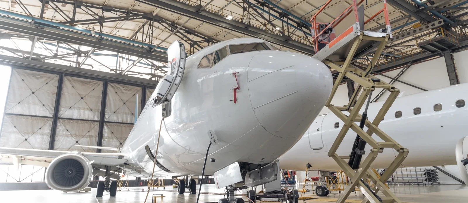 Jet airliner nose in a maintenance hangar beside a scissor lift platform