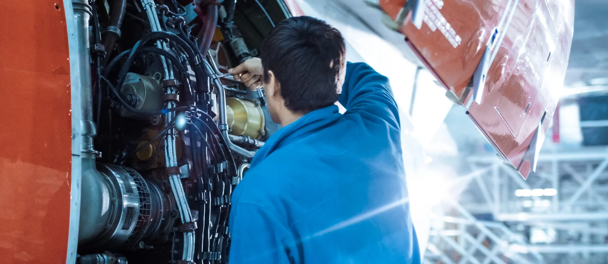 Aviation mechanic in a blue jacket working inside an open jet engine cowling