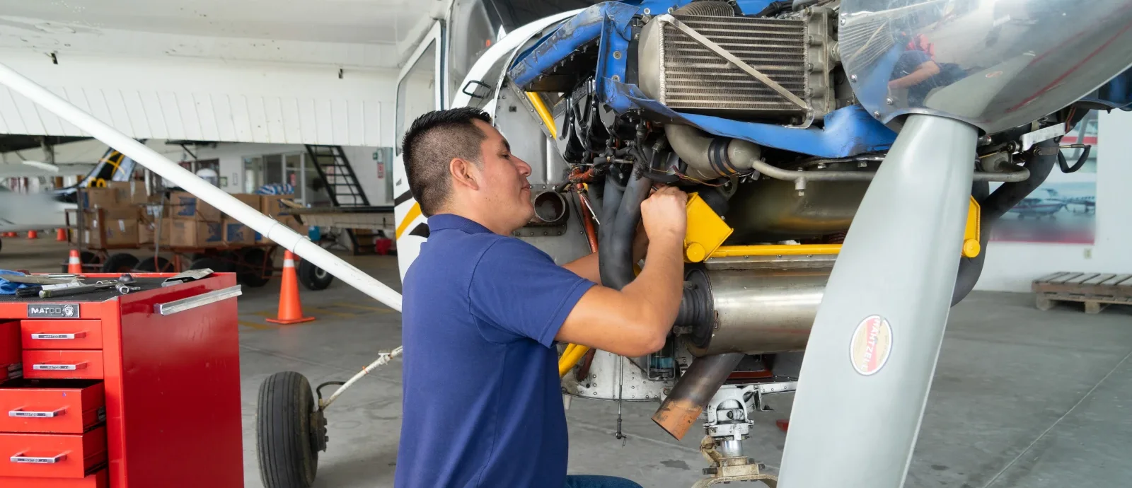 Aviation mechanic working on the piston engine of a high-wing single-engine airplane in a hangar