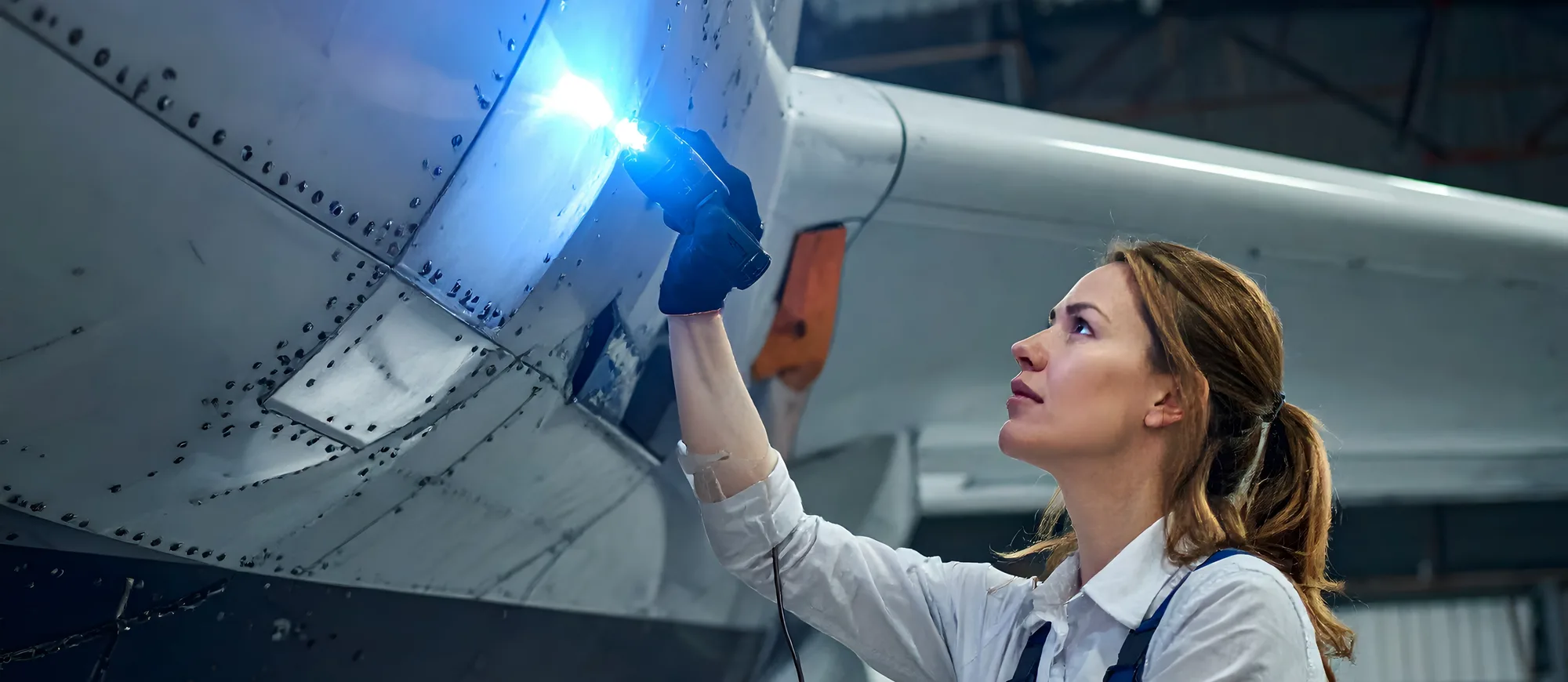 Aircraft maintenance technician inspecting an engine nacelle with a flashlight in a hangar