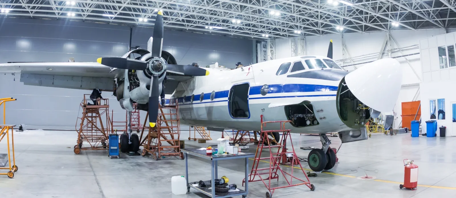 Twin-engine turboprop airplane on maintenance stands in a bright hangar, with its nose cone open